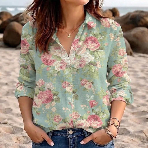 May include: A long-sleeve button-down shirt in a light sage green color featuring an all-over floral print with pink roses and white blossoms. The shirt has a classic collar, a front button placket, and is paired with blue denim jeans.