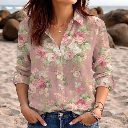 May include: A long-sleeved button-down shirt in a dusty pink hue featuring a repeating floral pattern of pink roses, white blossoms, and green leaves. The shirt has a classic collar, a front button placket, and is paired with blue denim jeans.