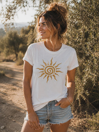 May include: A white short-sleeved t-shirt featuring a gold sun graphic with a spiral center and radiating wavy rays on the chest, paired with light blue denim shorts that have a frayed hemline and a classic five-pocket design.
