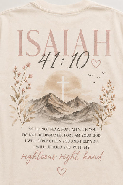 May include: A cream-colored t-shirt featuring a graphic print of mountains, a cross, and floral sprigs. The text reads: ISAIAH 41:10, SO DO NOT FEAR, FOR I AM WITH YOU; DO NOT BE DISMAYED, FOR I AM YOUR GOD. I WILL STRENGTHEN YOU AND HELP YOU; I WILL UPHOLD YOU WITH MY righteous right hand.