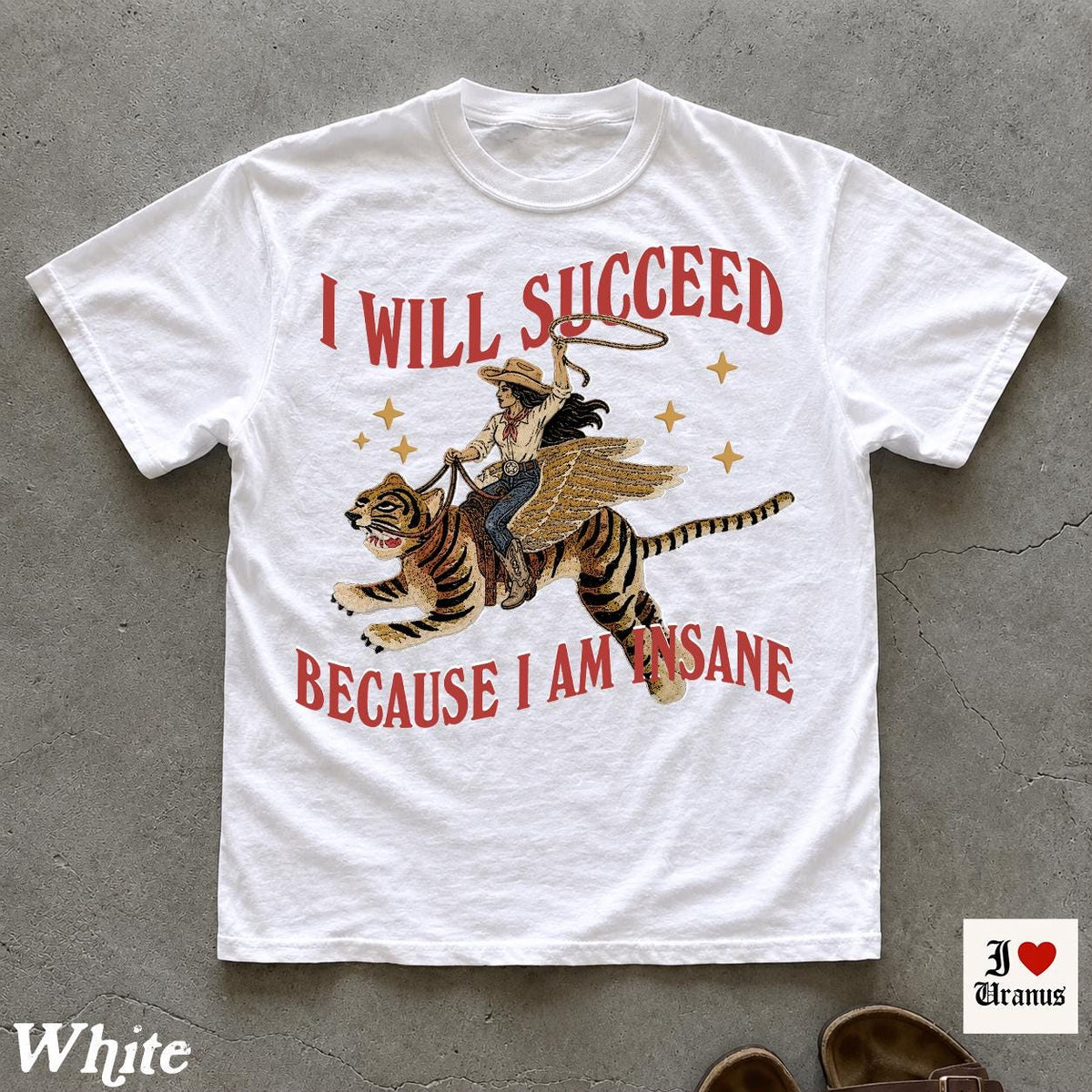 May include: A white short-sleeve t-shirt featuring a graphic of a person riding a winged tiger while holding a lasso. The text "I WILL SUCCEED" appears above the graphic, and "BECAUSE I AM INSANE" is printed below in red, stylized lettering.
