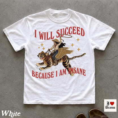 May include: A white short-sleeve t-shirt featuring a graphic of a person riding a winged tiger while holding a lasso. The text "I WILL SUCCEED" appears above the graphic, and "BECAUSE I AM INSANE" is printed below in red, stylized lettering.