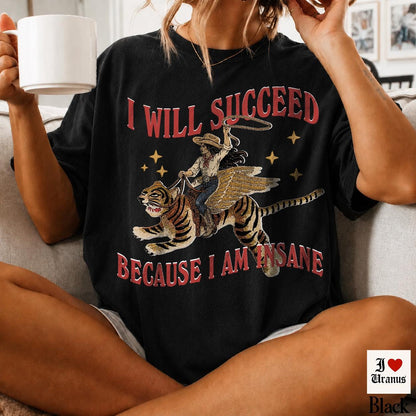 May include: A black short-sleeve t-shirt featuring a graphic of a person riding a winged tiger while holding a lasso. The text "I WILL SUCCEED" appears above the graphic and "BECAUSE I AM INSANE" appears below in red, stylized lettering.