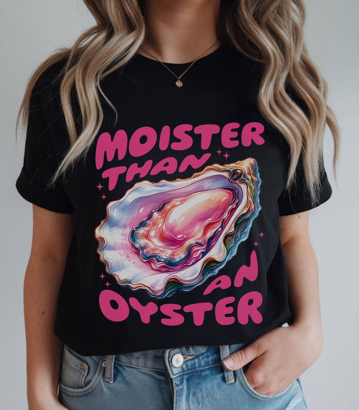 May include: A black short-sleeve t-shirt featuring a colorful graphic of an open oyster shell with pink, blue, and purple hues. The text "MOISTER THAN AN OYSTER" is printed in bold pink letters above and below the oyster illustration.