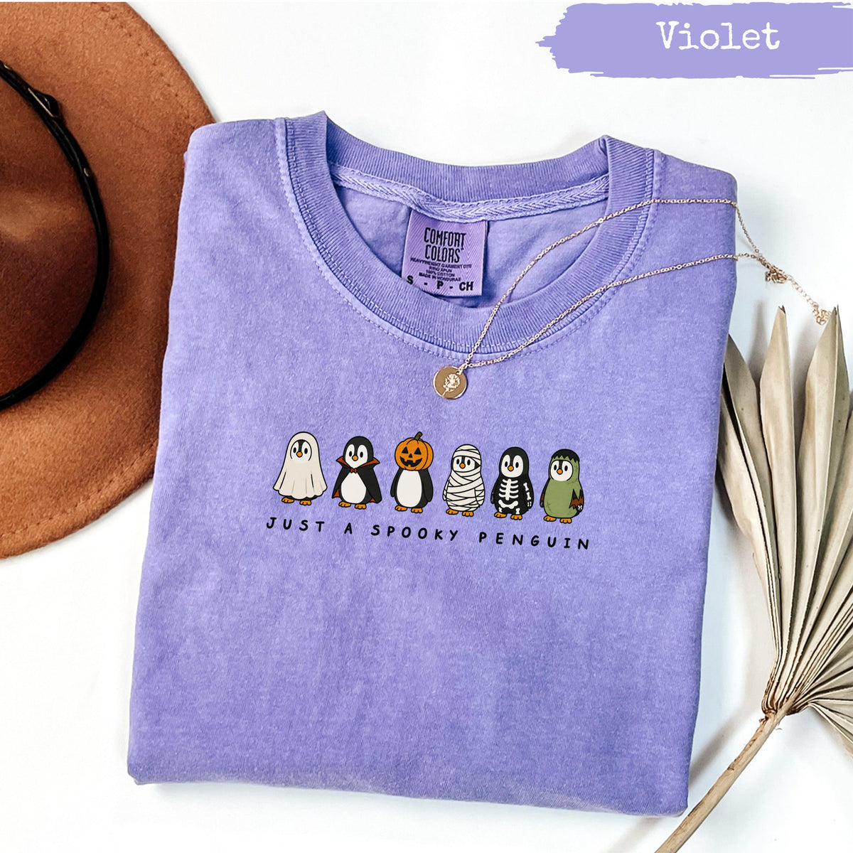 Purple Comfort Colors shirt with "Just a Spooky Penguin" text and Halloween penguins.