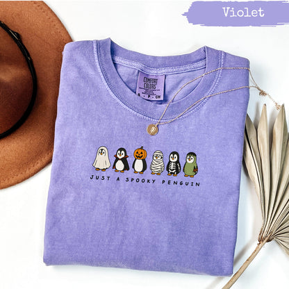 Purple Comfort Colors shirt with "Just a Spooky Penguin" text and Halloween penguins.
