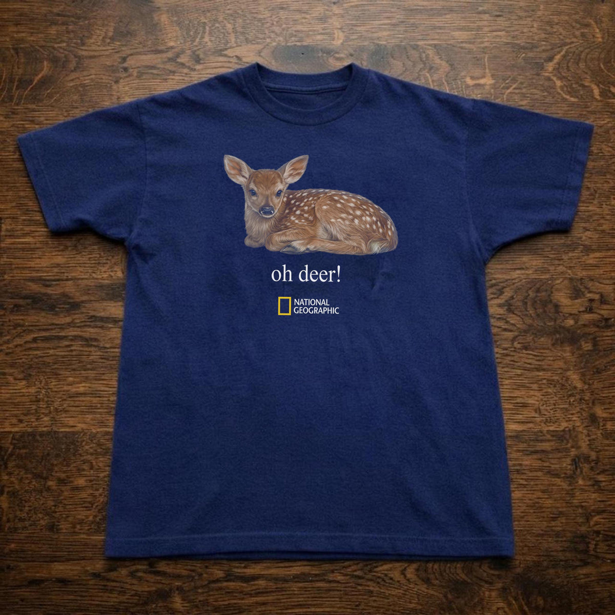 May include: A navy blue short-sleeve t-shirt featuring a graphic of a brown spotted fawn lying down. Below the fawn, the text reads "oh deer!" followed by the National Geographic logo in yellow and white.
