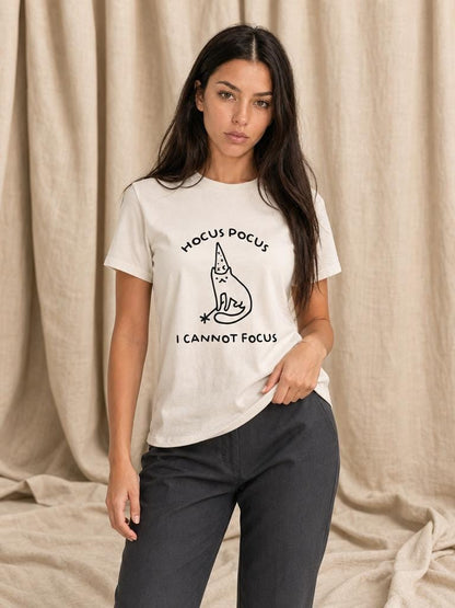 May include: A cream-colored short-sleeve t-shirt featuring a black line-art graphic of a cat wearing a wizard hat and holding a wand. The text above the cat reads HOCUS POCUS and the text below the cat reads I CANNOT FOCUS.