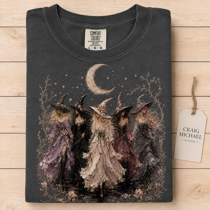 T-shirt graphic of five witches with magical hats and flowing dresses under a crescent moon.