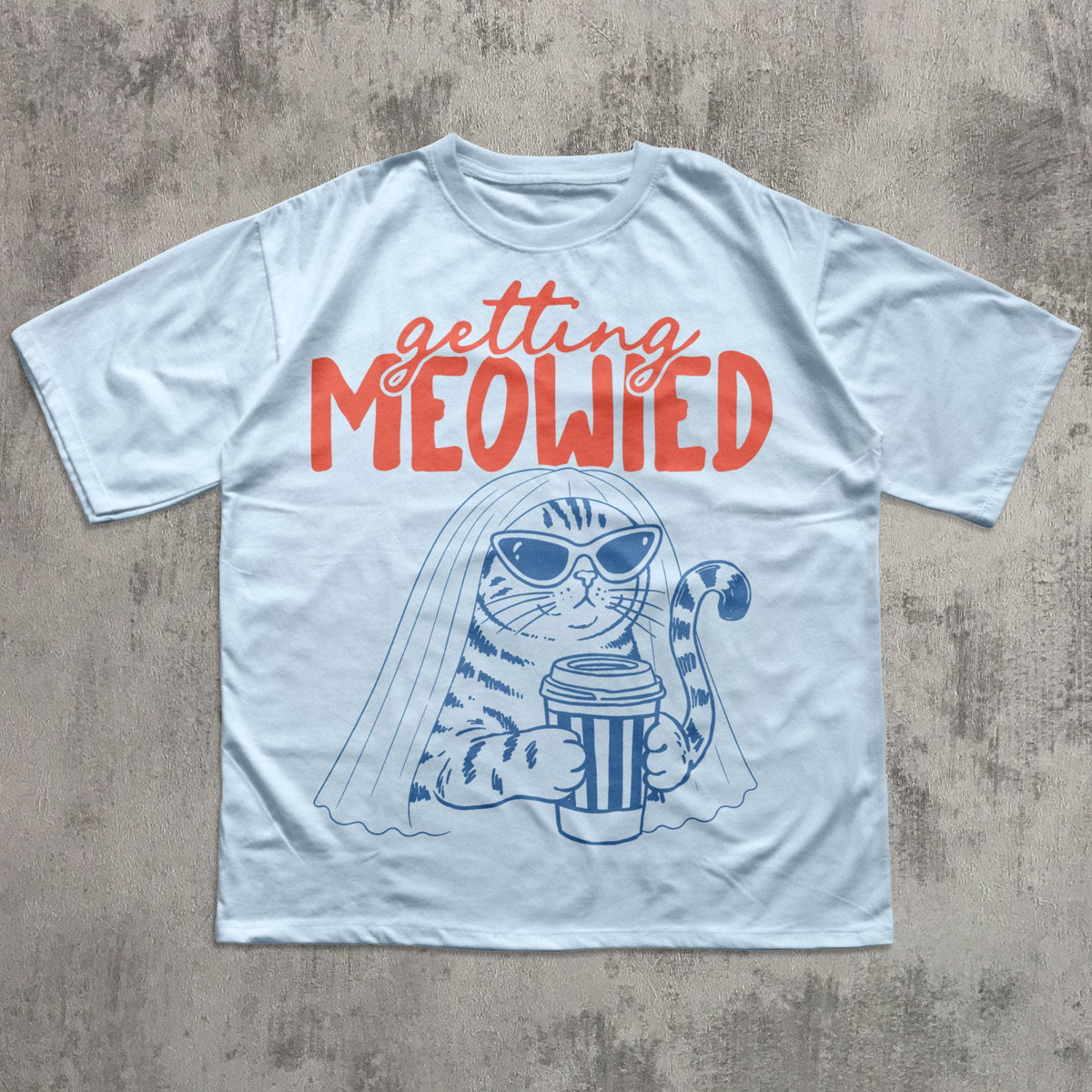 May include: A light blue t-shirt featuring a dark blue graphic of a cat wearing sunglasses and a veil while holding a coffee cup. Above the cat, the text "getting MEOWIED" is printed in a bold, orange, script and sans-serif font combination.