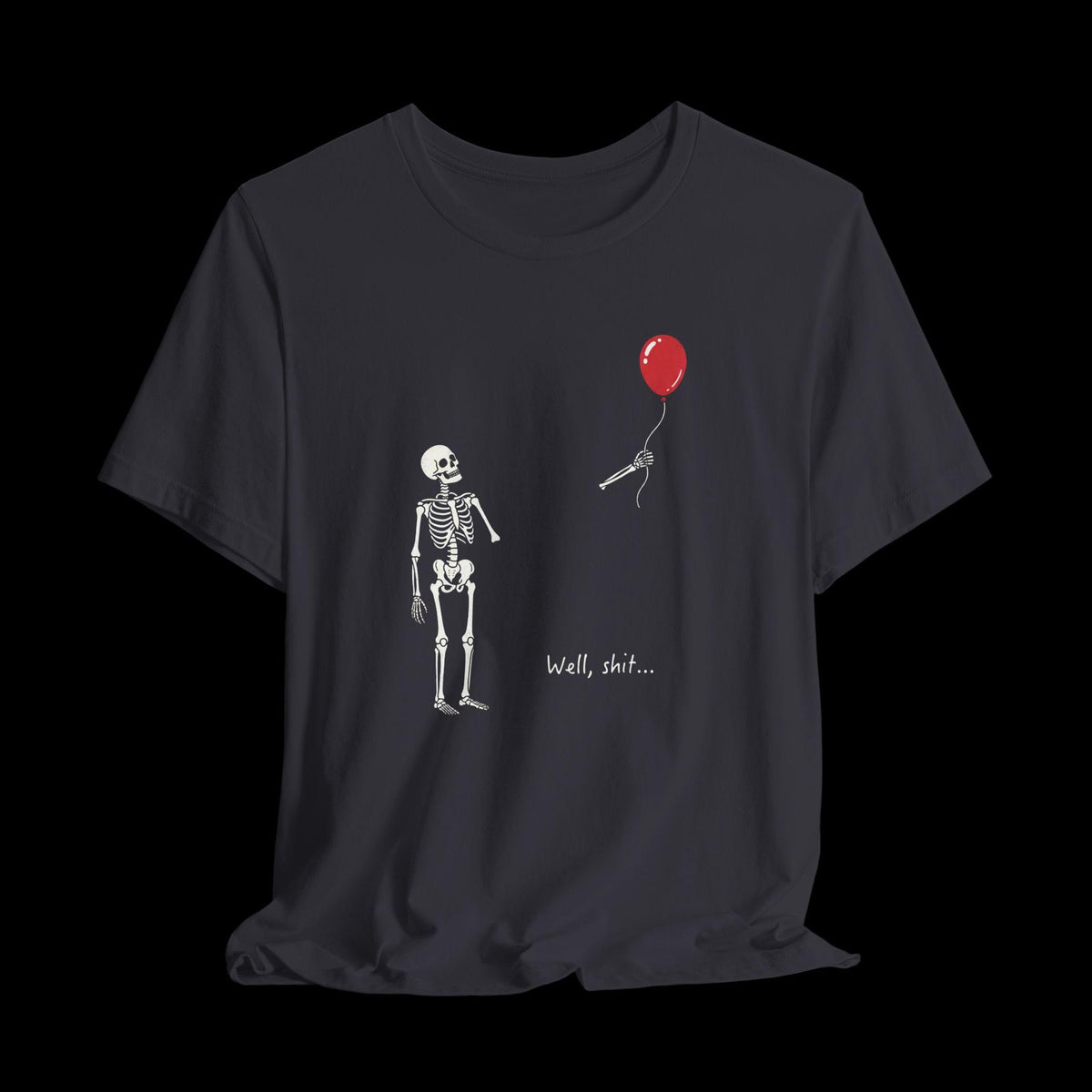 May include: A dark gray t-shirt featuring a white skeleton graphic looking at a detached skeletal hand holding a red balloon. The text "Well, shit..." is printed in white below the hand. The design is centered on the front of the shirt.