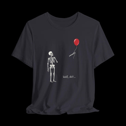 May include: A dark gray t-shirt featuring a white skeleton graphic looking at a detached skeletal hand holding a red balloon. The text "Well, shit..." is printed in white below the hand. The design is centered on the front of the shirt.