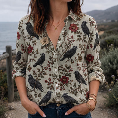 May include: A long-sleeve button-down shirt in a light beige color featuring a repeating pattern of black crows perched on branches with dark red and muted yellow flowers. The shirt has a classic collar and white buttons down the front placket.