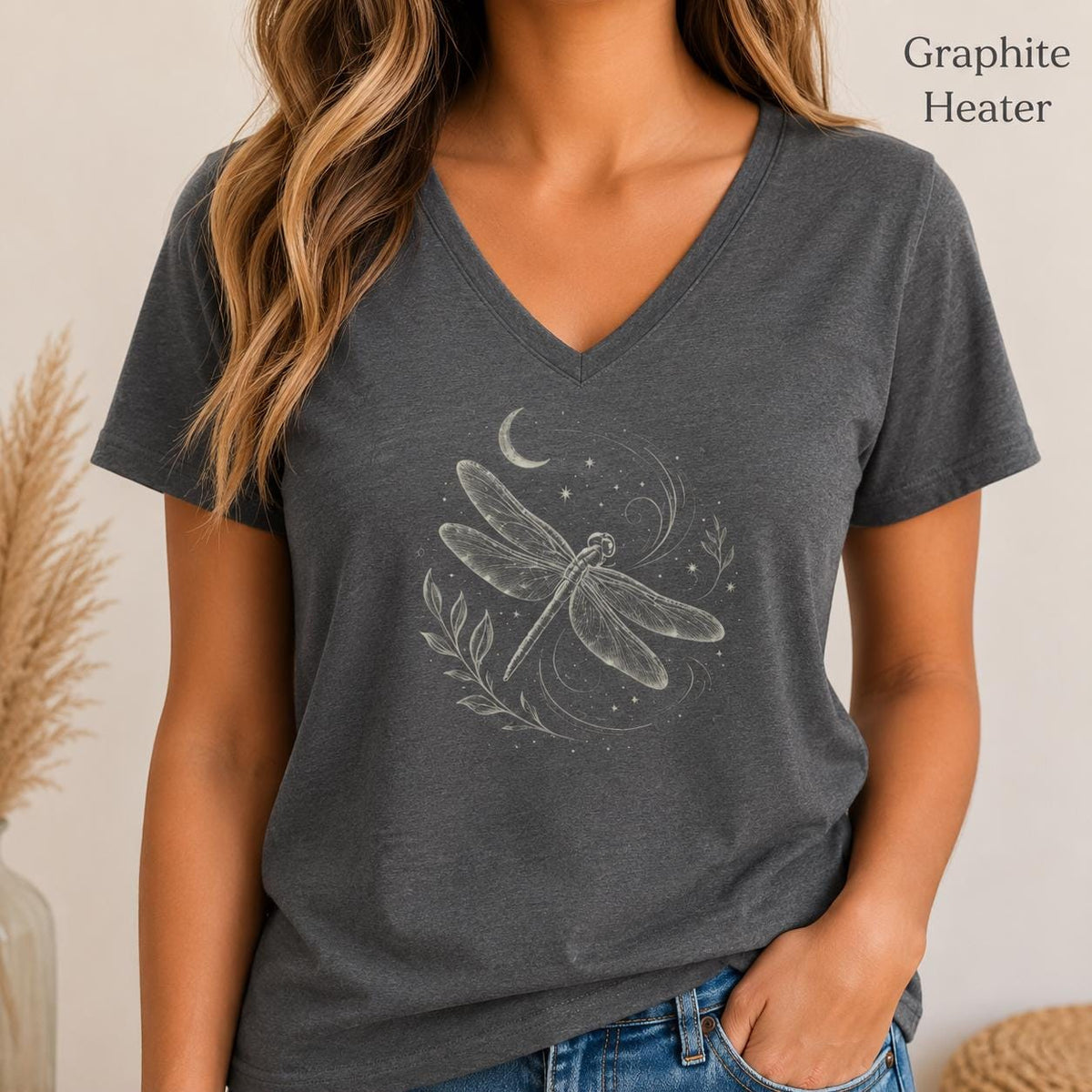 May include: A graphite heather V-neck t-shirt featuring a white line art graphic of a dragonfly, a crescent moon, and small stars. The text Graphite Heater is printed in the upper right corner of the image above the short-sleeved shirt.