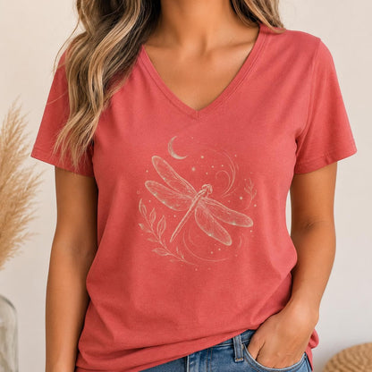 May include: A short-sleeved, V-neck t-shirt in a muted terracotta red color. The center of the shirt features a light-colored graphic print of a dragonfly surrounded by delicate swirling lines, small stars, a crescent moon, and a leafy branch.