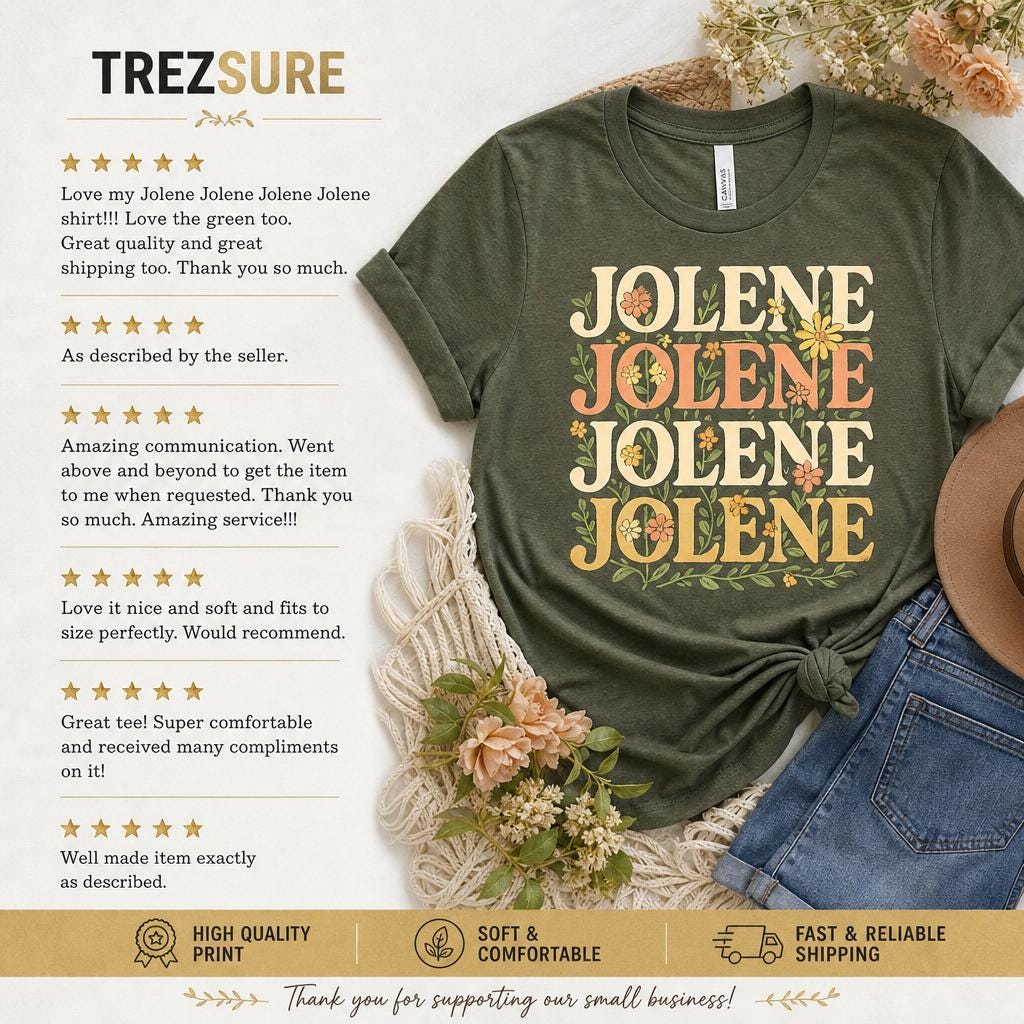 May include: An olive green short-sleeve t-shirt featuring the text JOLENE repeated four times in a stacked, retro-style font, decorated with small orange and yellow flowers and green leaves. The shirt is displayed alongside blue denim shorts.