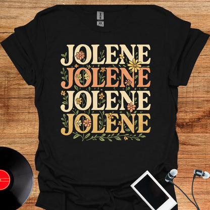 May include: A black short-sleeved t-shirt featuring the word JOLENE printed four times in a stacked layout. The text is rendered in a cream-colored serif font and is surrounded by small, colorful floral illustrations in shades of yellow and orange.