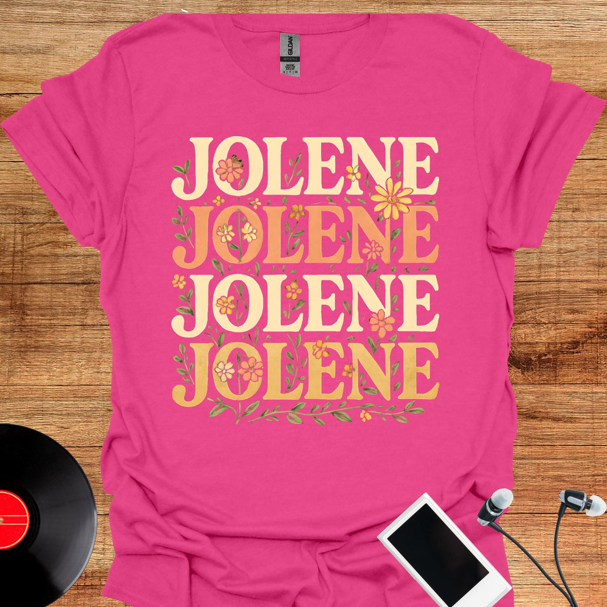 May include: A bright pink short-sleeved t-shirt featuring the word JOLENE printed four times in a stacked, cream-colored serif font. The text is decorated with small, colorful floral illustrations in shades of yellow, orange, and green.