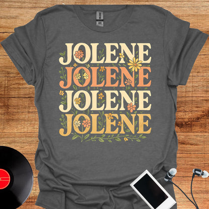May include: A dark gray short-sleeve t-shirt featuring the name JOLENE printed four times in a stacked layout. The text is rendered in a bold, serif font with alternating cream and orange colors, surrounded by small green leaves and flowers.