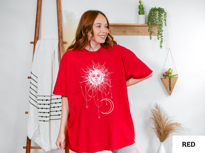 May include: A bright red short-sleeved t-shirt featuring a large white graphic print on the front. The design depicts a stylized sun with a human face surrounded by radiating rays, with dangling chains, small stars, and a crescent moon below it.