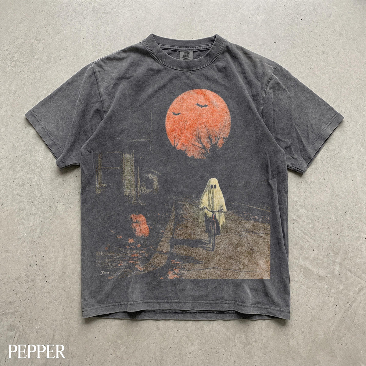 May include: A charcoal gray short-sleeve t-shirt featuring a graphic print of a ghost riding a bicycle under a large orange moon. The design includes silhouettes of bats, bare tree branches, and a pumpkin on a path, with the word PEPPER at the bottom.