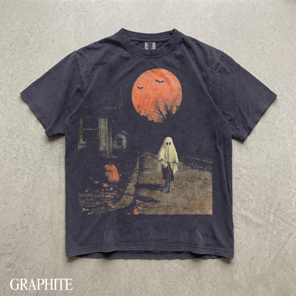 May include: A graphite-colored short-sleeve t-shirt featuring a graphic print of a ghost riding a bicycle on a path at night. The scene includes a large orange moon, silhouettes of bare trees, flying bats, and a house. The text Blossom Trendy is visible.
