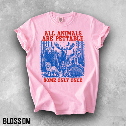 May include: A light pink short-sleeve t-shirt featuring a blue graphic of a bear, moose, wolf, fox, raccoon, and porcupine in a forest. The red text reads ALL ANIMALS ARE PETTABLE and SOME ONLY ONCE. The shirt has a crew neckline and short sleeves.