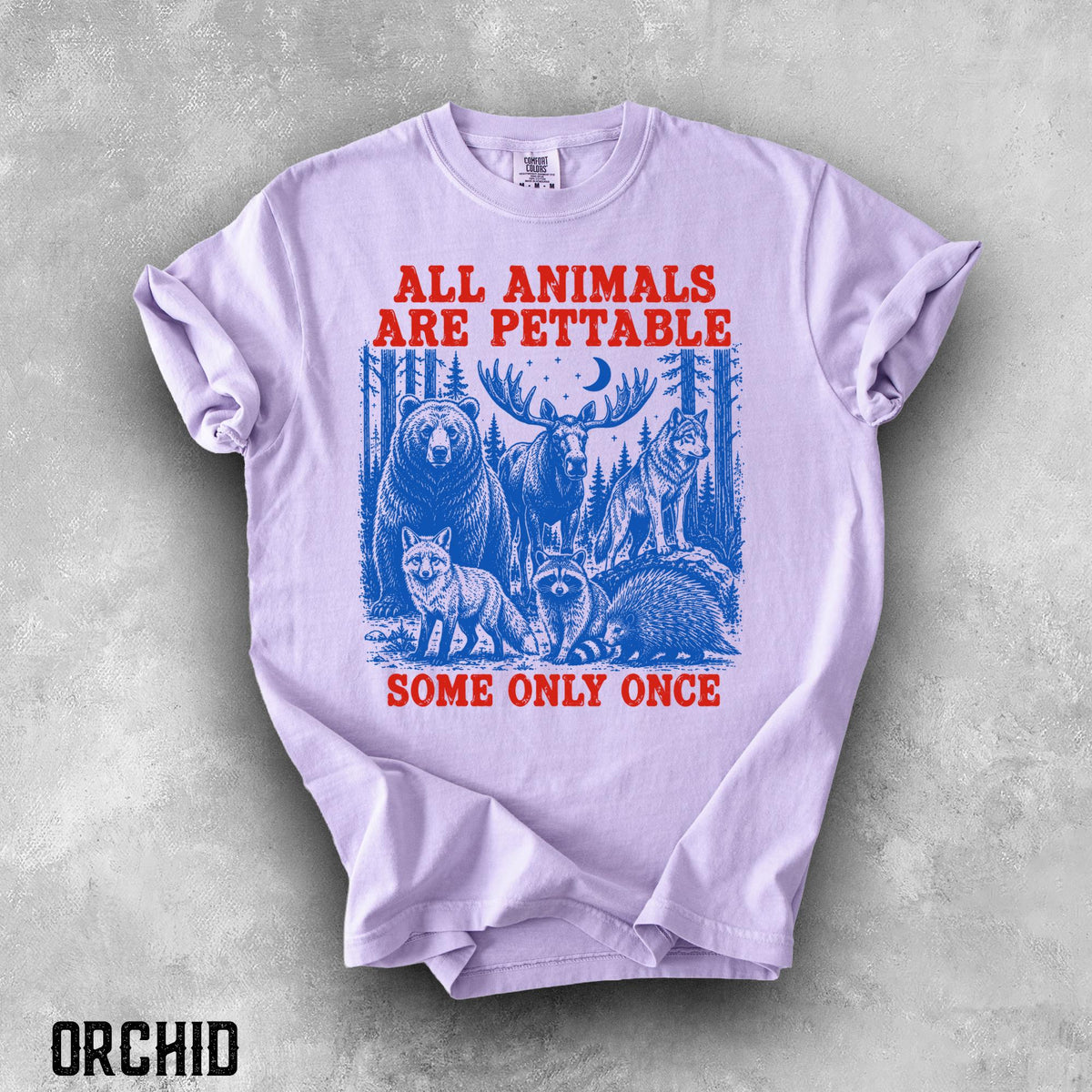 May include: A light purple short-sleeve t-shirt featuring a blue graphic of a bear, moose, wolf, fox, raccoon, and porcupine in a forest. The red text reads ALL ANIMALS ARE PETTABLE at the top and SOME ONLY ONCE at the bottom of the graphic.