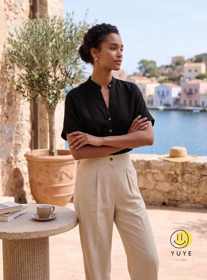 May include: A black short-sleeved shirt with a mandarin collar and a front button placket, paired with high-waisted beige trousers featuring front pleats. The shirt has a relaxed fit, and the trousers have a straight-leg cut with a button closure.