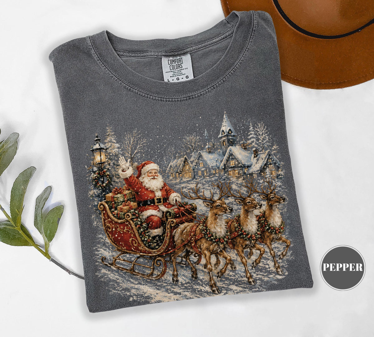 May include: A charcoal gray short-sleeve t-shirt featuring a graphic print of Santa Claus in a red sleigh pulled by three reindeer. The scene includes a snowy village with a church and a streetlamp. The shirt has a Comfort Colors brand label.