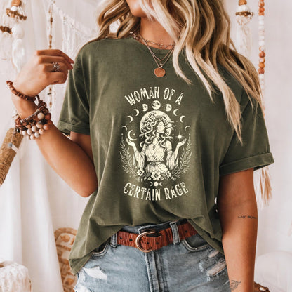 May include: An olive green short-sleeve t-shirt featuring a cream-colored graphic print of a figure with snake-like hair, surrounded by moon phases, stars, and foliage. The text reads "WOMAN OF A CERTAIN RAGE" in a distressed, arched font.