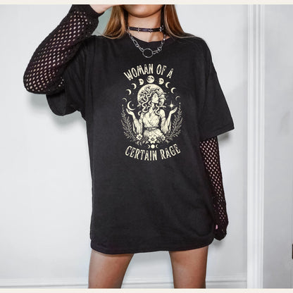 May include: A black short-sleeved t-shirt featuring a cream-colored graphic of a figure with snake-like hair, surrounded by moon phases and foliage, with the text "WOMAN OF A CERTAIN RAGE" printed in a curved arch above and below the illustration.