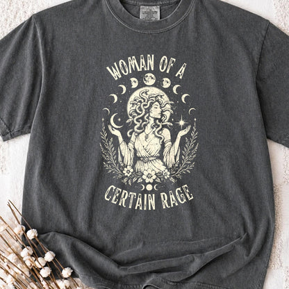 May include: A charcoal gray t-shirt featuring a cream-colored graphic of a figure with snakes for hair, surrounded by moon phases, stars, and foliage. The text "WOMAN OF A CERTAIN RAGE" is printed in a curved font above and below the central illustration.