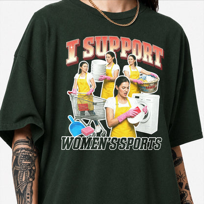 May include: A dark green t-shirt featuring a graphic print with the text I SUPPORT WOMEN'S SPORTS. The design shows a person in a yellow apron and pink gloves performing household chores like laundry, dishwashing, and shopping with a cart.