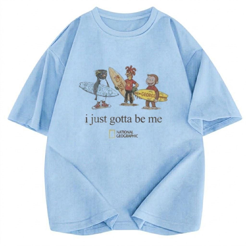May include: A light blue short-sleeve t-shirt featuring a graphic of a penguin, a chicken, and a monkey holding surfboards. The text "i just gotta be me" is printed below the characters, followed by the National Geographic logo in yellow and white.