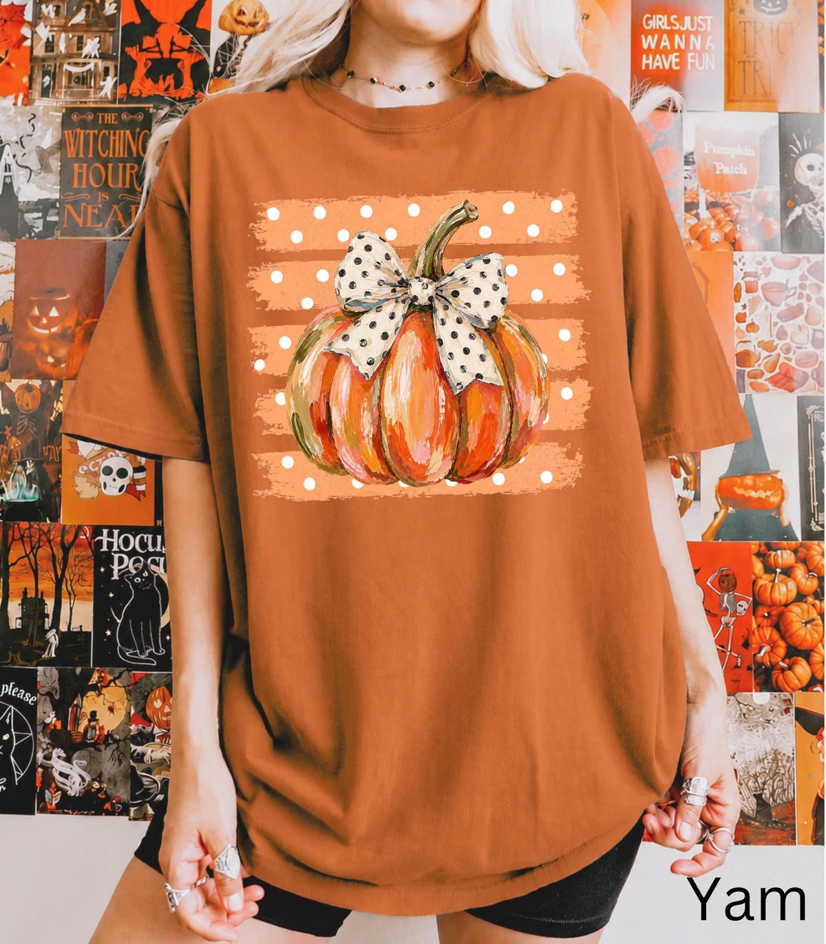 May include: A burnt orange t-shirt featuring a graphic of a painted pumpkin with a white and black polka dot bow. The pumpkin is centered over a rectangular background of horizontal orange stripes and white polka dots on the front of the shirt.