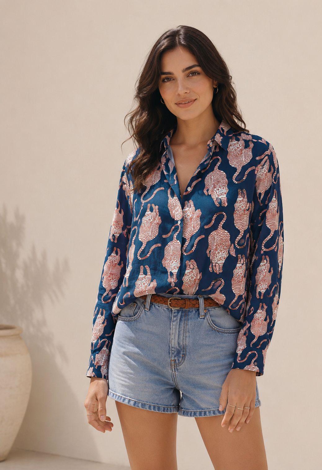 May include: A long-sleeved button-down shirt in deep blue featuring a repeating pattern of orange and white tigers, paired with light blue denim shorts and a thin brown woven leather belt with a metal buckle at the waistline.