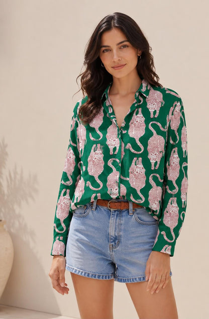 May include: A long-sleeved button-down shirt in a vibrant green color featuring a repeating pattern of stylized red tigers. The shirt has a classic collar and is paired with light blue denim shorts and a brown leather belt with a metal buckle.
