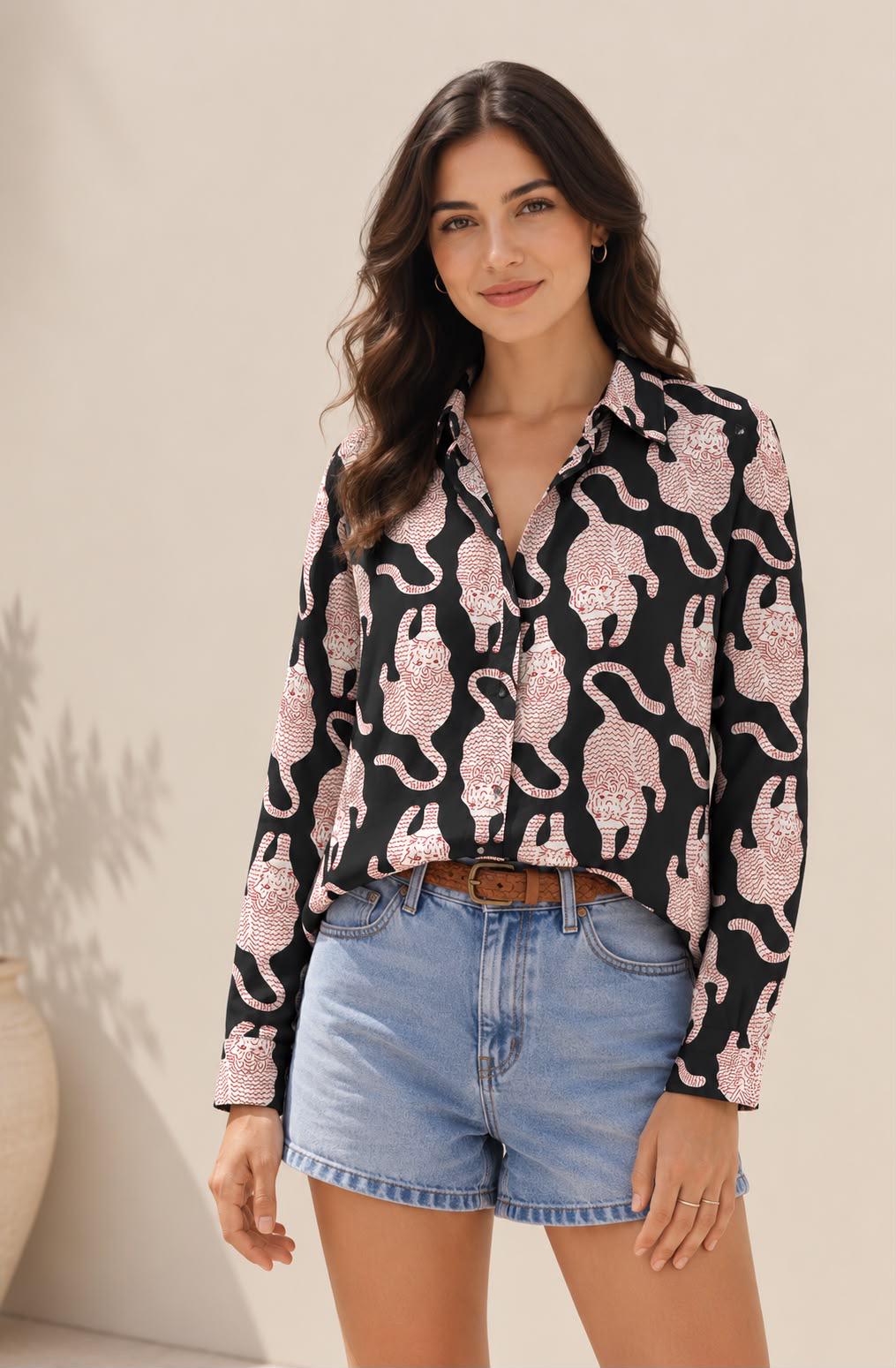May include: A long-sleeved button-down shirt in black featuring a repeating pattern of stylized tigers in a light red or pinkish hue. The shirt has a classic collar and is tucked into light blue denim shorts with a brown leather belt.