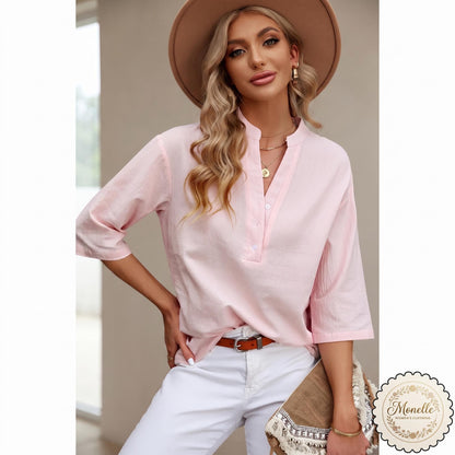 May include: A light pink, long-sleeved blouse with a mandarin collar and a partial button-down front placket. The shirt is paired with white pants and a brown belt with a silver buckle. A tan wide-brimmed hat is worn on the head.
