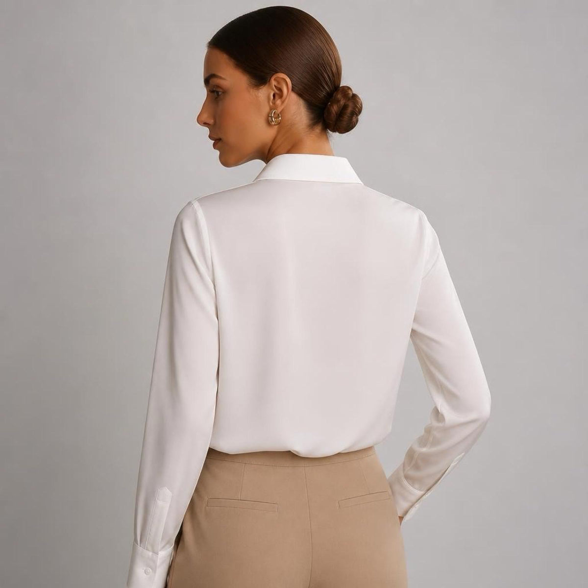 May include: A long-sleeved, off-white button-down shirt with a classic collar, featuring a smooth, satin-like finish. The shirt is tucked into a pair of solid tan trousers, showcasing a clean, tailored fit with visible stitching at the waist.
