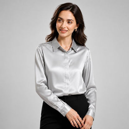 May include: A long-sleeved button-down shirt in a lustrous silver satin fabric. The shirt features a classic pointed collar, a concealed front button placket, and structured cuffs with a single button closure, paired with black trousers.