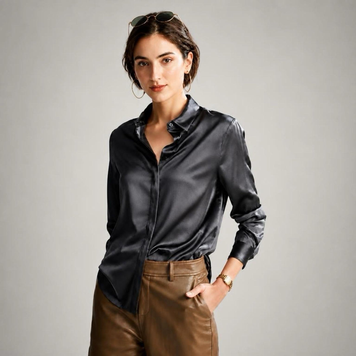 May include: A long-sleeved black satin button-down shirt with a pointed collar and a smooth, reflective finish, paired with brown leather trousers featuring a high waist and a visible button closure at the center front of the waistband.