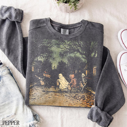 May include: A charcoal gray crewneck sweatshirt featuring a vintage-style graphic of four children in Halloween costumes, including a witch, a ghost, a pumpkin, and a skeleton, walking down a tree-lined street at night with a faded, textured print.