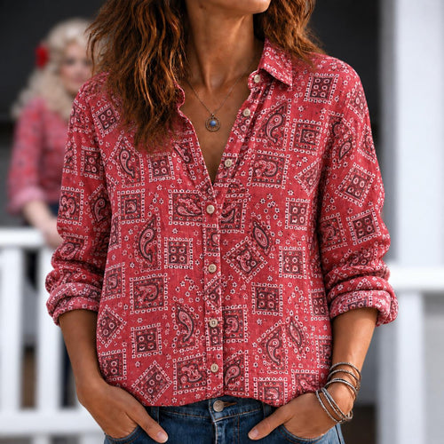 May include: A long-sleeved button-down shirt in a vibrant red hue, featuring a repeating pattern of dark paisley motifs and geometric squares. The shirt has a classic collar, a front button placket, and is paired with blue denim jeans.