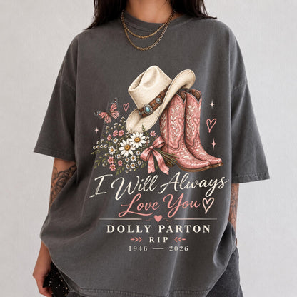 May include: A charcoal gray t-shirt featuring a graphic of a beige cowboy hat, pink cowboy boots, a butterfly, and a bouquet of daisies. The text reads I Will Always Love You, Dolly Parton, RIP, and the years 1946 - 2026, with small pink hearts.