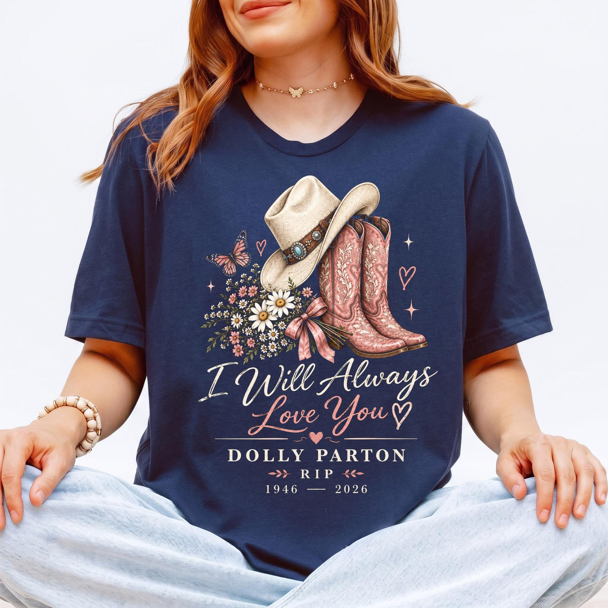 May include: A navy blue t-shirt featuring a graphic of a cowboy hat, pink cowboy boots, a bouquet of daisies, and a butterfly. The text reads I Will Always Love You, DOLLY PARTON, RIP, and the years 1946-2026, accented with small hearts and stars.