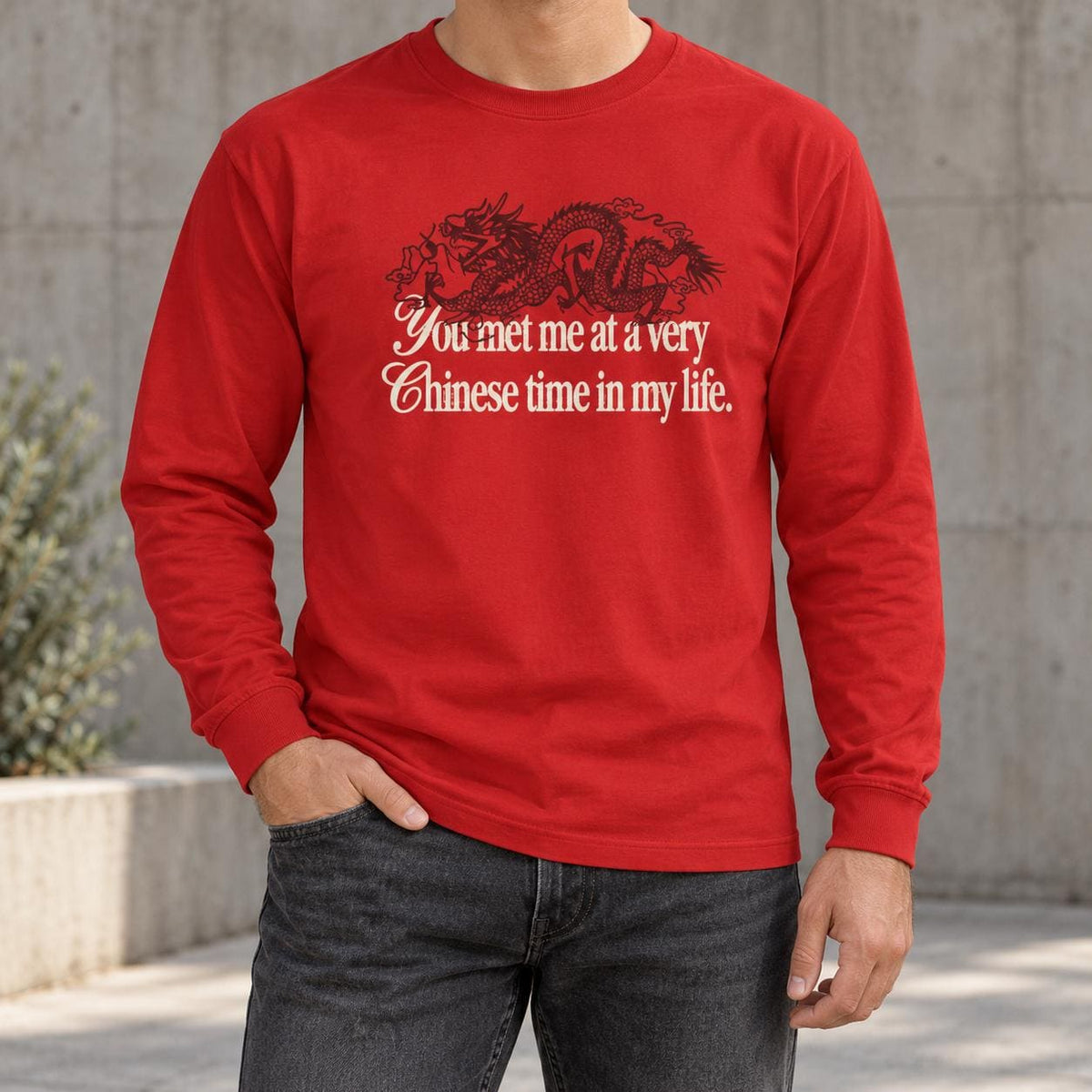 May include: A bright red long-sleeve shirt featuring a black graphic of a dragon positioned above the white text that reads, You met me at a very Chinese time in my life. The shirt has a crew neckline and long sleeves with ribbed cuffs.