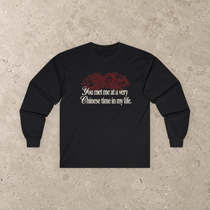 May include: A black long-sleeve shirt featuring a dark red dragon graphic positioned above the white text that reads, "You met me at a very Chinese time in my life." The shirt has a crew neckline and long sleeves with ribbed cuffs, presenting a simple design.