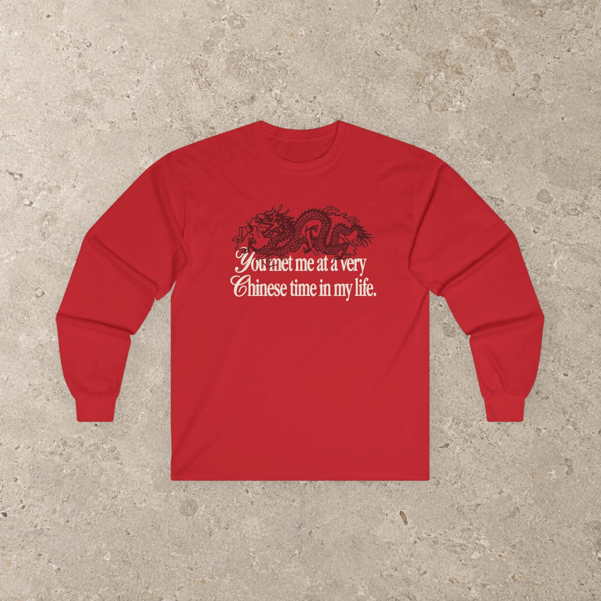 May include: A bright red long-sleeve shirt featuring a black graphic of a dragon positioned above the white text that reads, You met me at a very Chinese time in my life. The shirt has a crew neckline and long sleeves with ribbed cuffs.
